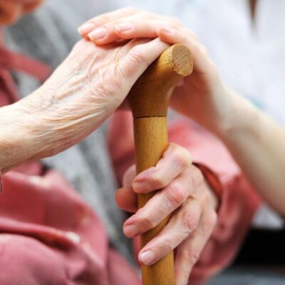 Elderly woman's hand on cane, caregiver's support.