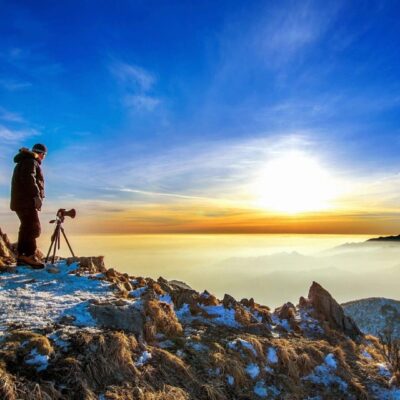 A man standing on top of a mountain with a tripod.