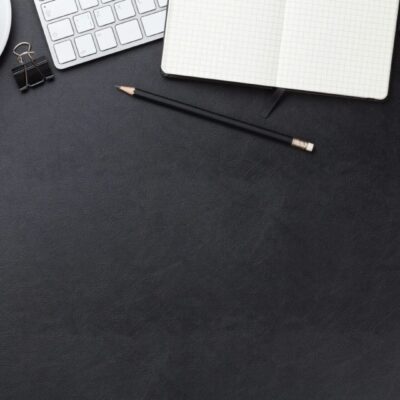 Top view of a black desk with a cup of coffee and a notebook.