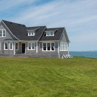 A gray house sits on a grassy hill overlooking the ocean.