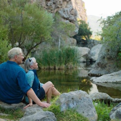 An older couple sitting on rocks near a pond.