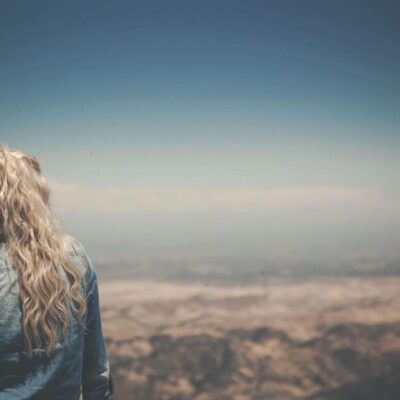 A woman with long blonde hair standing on top of a mountain.