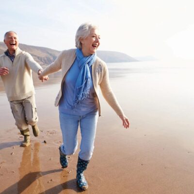 An older couple running on the beach.