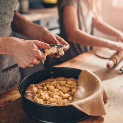 Hands peeling ginger over a bowl filled with peeled ginger pieces.