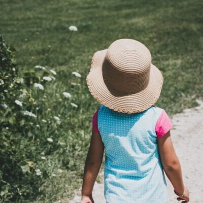 A little girl walking down a dirt path with a hat on.
