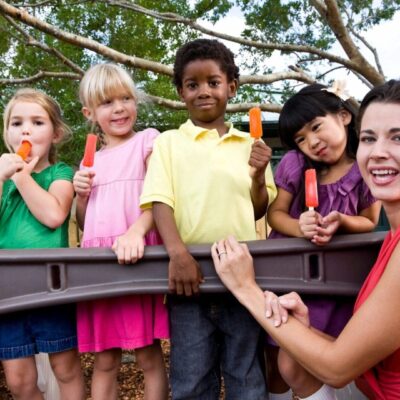 A woman holding carrots with children on a playground.