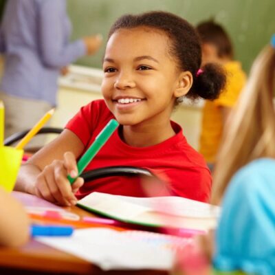 Smiling girl coloring in classroom.