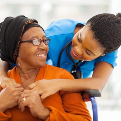 A nurse hugs an elderly woman in a wheelchair.