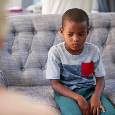 A young boy sitting on a couch looking thoughtful and serious.