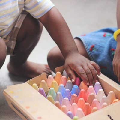 Children's hands reaching for colorful chalks.