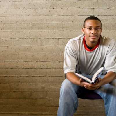 Man sitting on chair, holding open book.