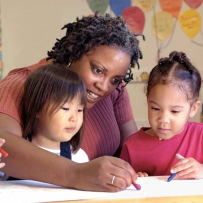 A woman and two children sitting at a table with crayons.