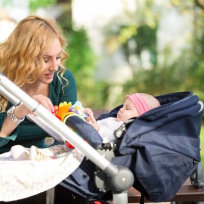 A woman is sitting on a bench with her baby in a stroller.