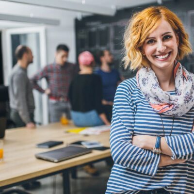 A smiling woman standing in an office with her arms crossed.