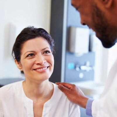 A woman smiling warmly at a man who has his hand on her shoulder.