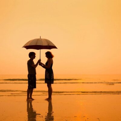 Silhouette couple sharing umbrella on beach.
