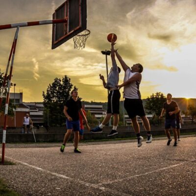 A group of people playing basketball at sunset.