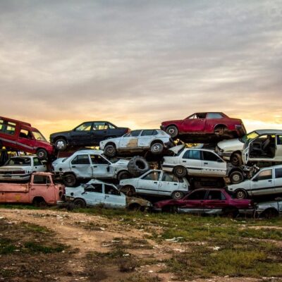 A pile of old cars in a field at sunset.