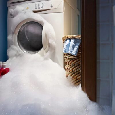 Washing machine overflowing with foam in a laundry room.