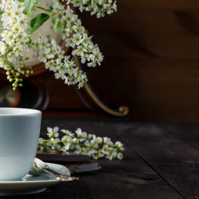 White teacup, saucer, flowers, dark wood.