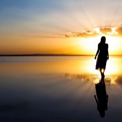 A silhouette of a woman walking in the water at sunset.