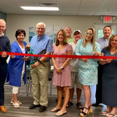A group of people cutting a ribbon in an office.