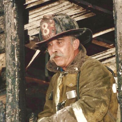 A firefighter standing in the window of an old house.