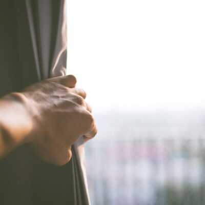 A hand reaching out of a window to open a curtain.