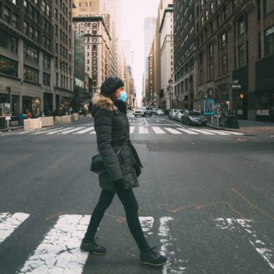 A woman wearing a face mask crossing a street in new york city.