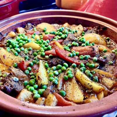 A clay pot with meat, vegetables, and peas.