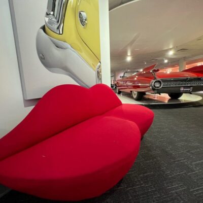 A red couch sits in front of a car in a museum.