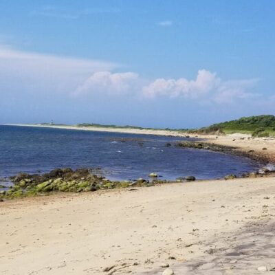 Sandy beach, ocean, and distant lighthouse.